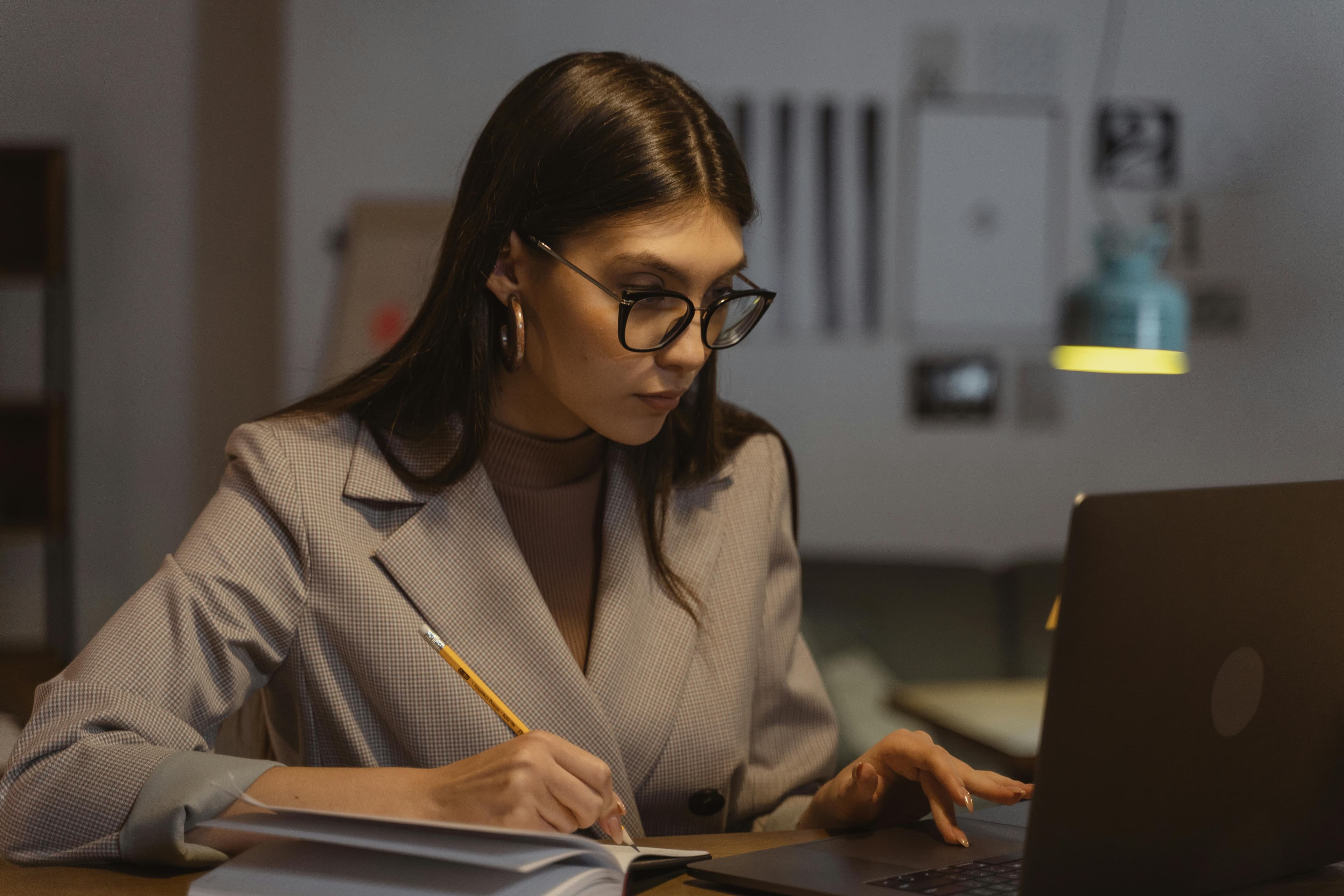 Manager donna concentrata alla scrivania con laptop e notebook in un ufficio luminoso, impegnata in un lavoro strategico di pianificazione e crescita professionale